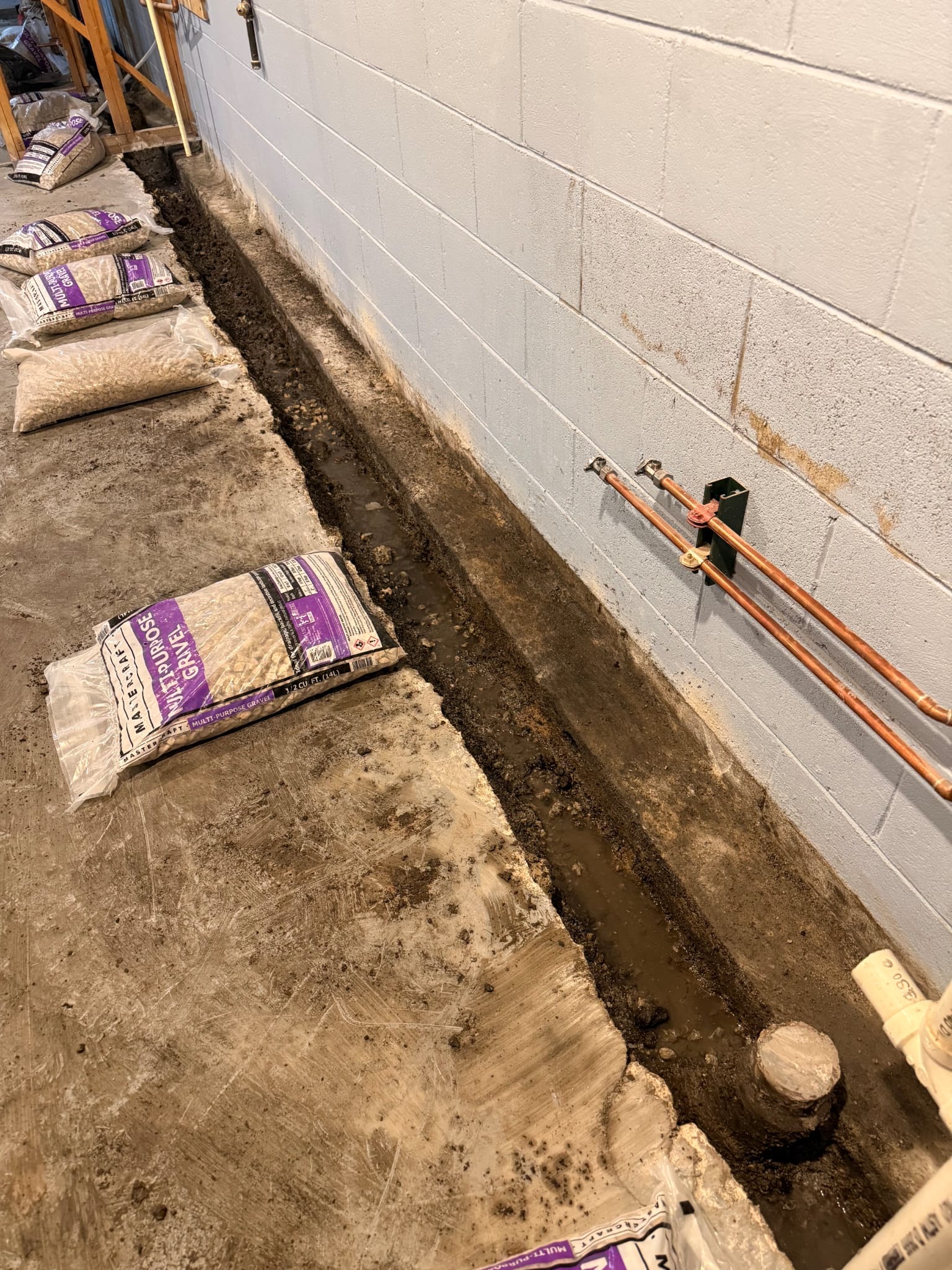 Before — water pooling in an open perimeter trench along a damp basement foundation wall